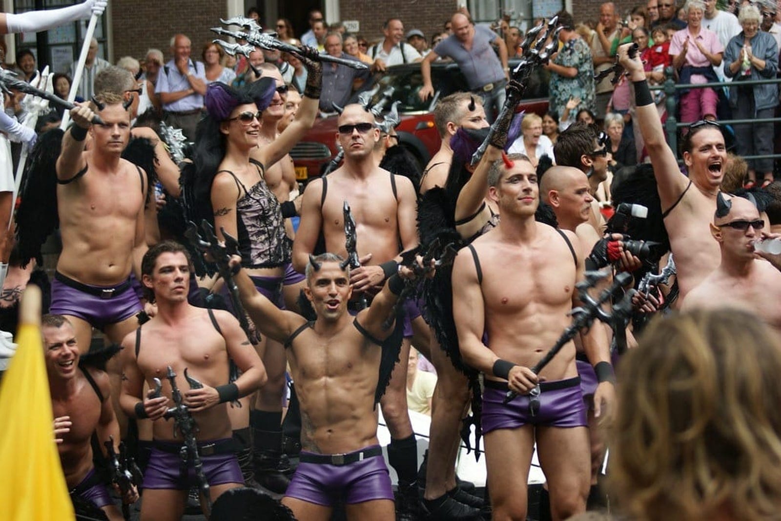 Rue du quartier gay d'Amsterdam en soirée, terrasses éclairées et passants le long des façades étroites.