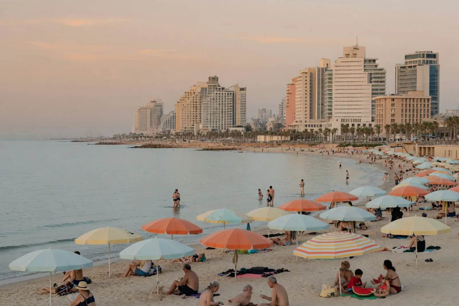 Baigneurs et parasols sur la plage nord de Tel Aviv, tours d'hôtels en arrière-plan, mer calme en fin d'après-midi.