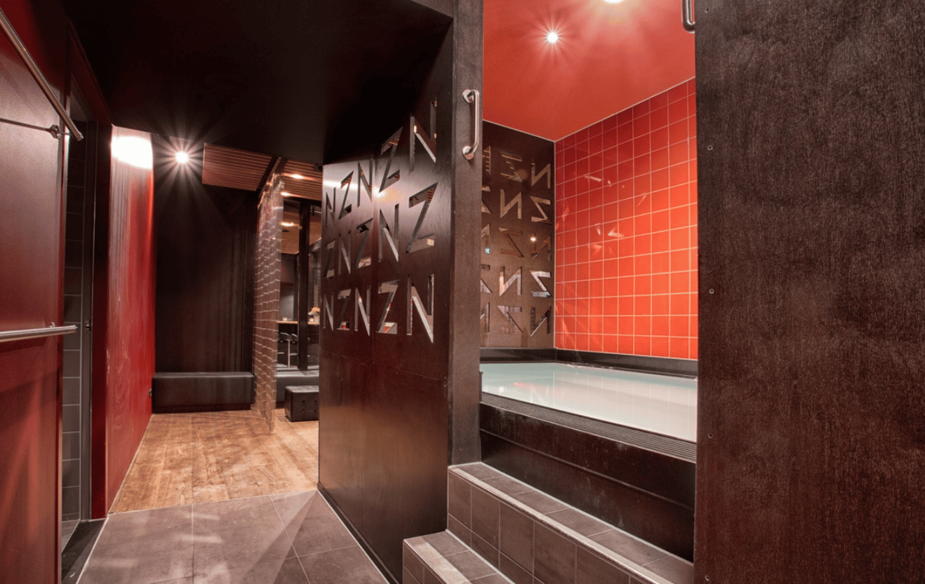 Intérieur d'un sauna gay urbain : espace de détente carrelé, lumière tamisée, banquettes et couloirs menant aux salles de chaleur.