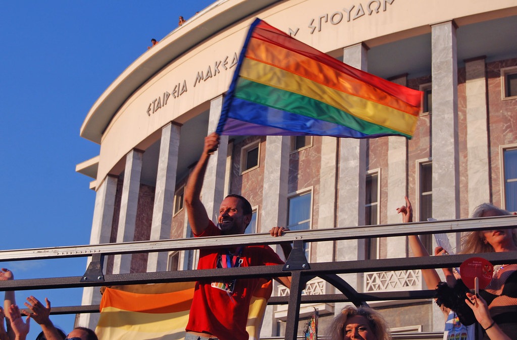 Un homme participant à des événements LGBTQ+ en Grèce agitant fièrement un drapeau arc-en-ciel.