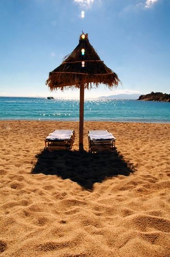 Deux chaises longues sur la plage avec un parasol en chaume, dans les plages gay-friendly de Grèce.