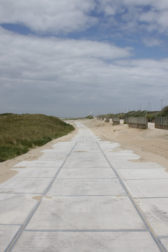 Une route en béton menant à une plage de sable en Belgique avec des paysages côtiers spectaculaires.
