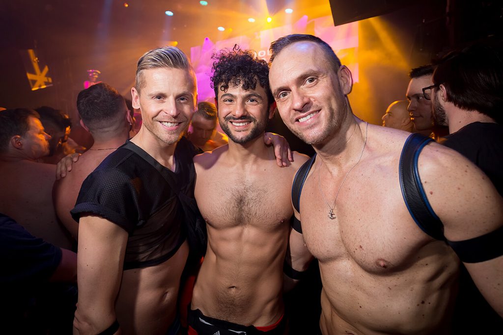 Trois hommes torse nu posant pour une photo dans une boîte de nuit gay à Amsterdam.