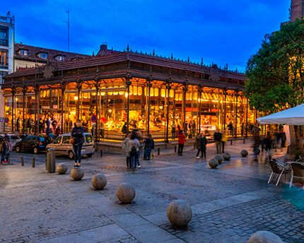 Une place animée de la ville la nuit avec des habitants et des touristes explorant les meilleurs bars à tapas de Madrid.