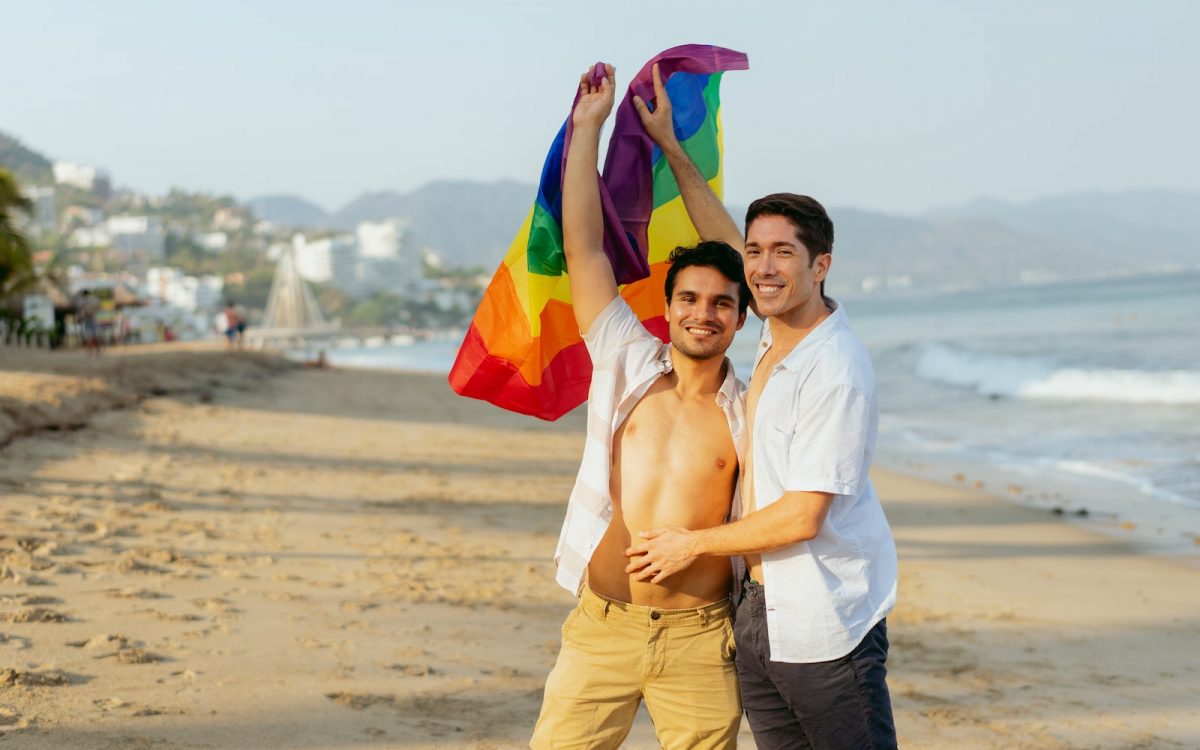 A Couple Holding a Rainbow Flag at the Beach